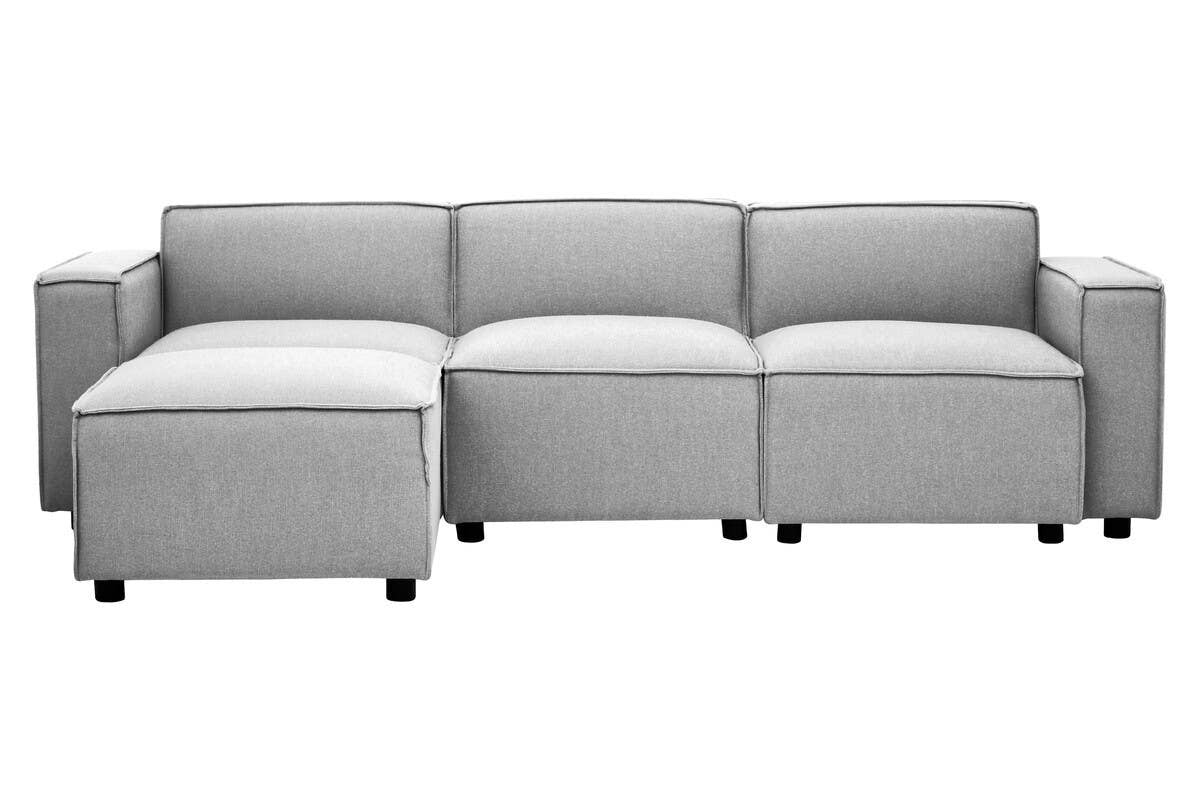 Grey fabric modular ottoman featuring a sleek design with clean lines and a low profile. The ottoman has a soft, upholstered surface and is supported by small, round legs. It consists of multiple sections that can be arranged in various configurations for versatile use in living spaces