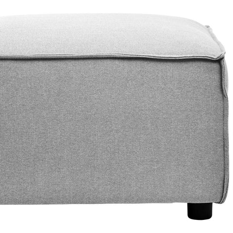 Grey fabric modular ottoman with a textured surface and a clean, modern design. The ottoman features a slightly rounded edge and rests on small black legs, providing a contemporary look suitable for various home decor styles