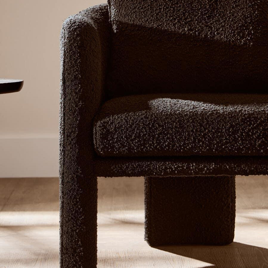 Textured black armchair with boucle upholstery on wooden floor in natural light