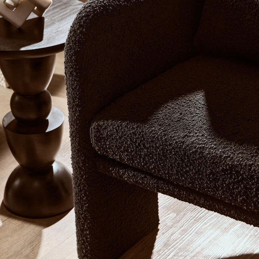 Textured brown armchair beside dark wood side table with modern decor accent