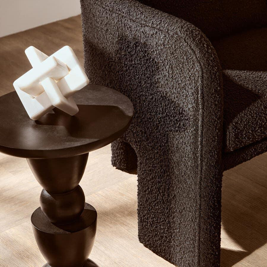 Curved black boucle armchair beside modern dark wood side table with white sculpture