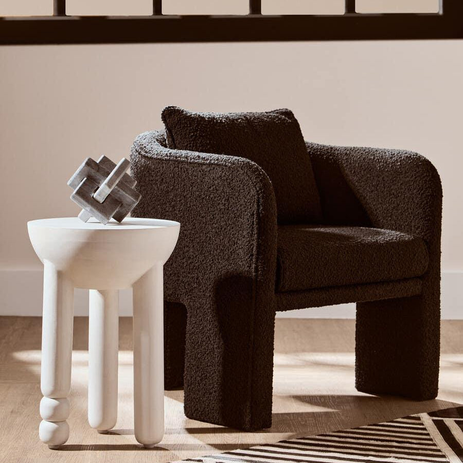 Black boucle armchair with cushion beside sculpted white side table on striped rug