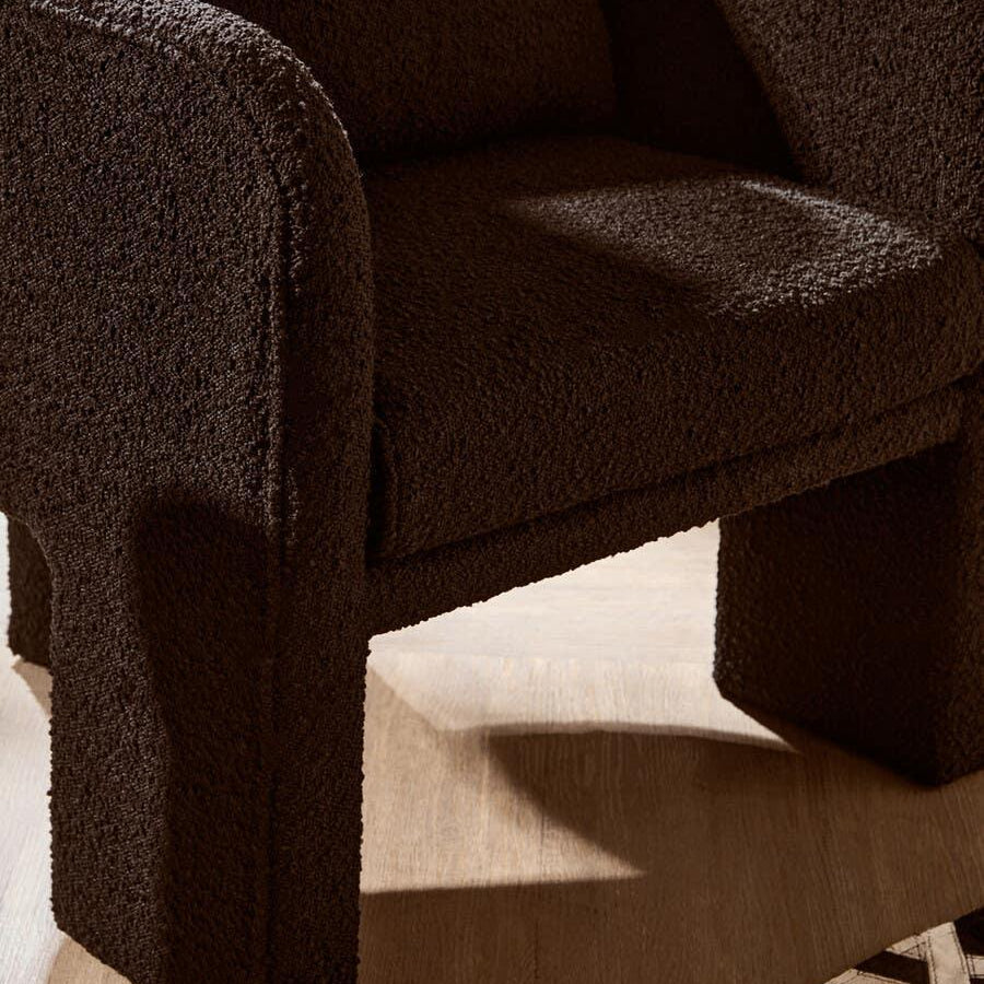 Brown textured armchair with rounded arms and plush seat on wooden floor beside geometric rug