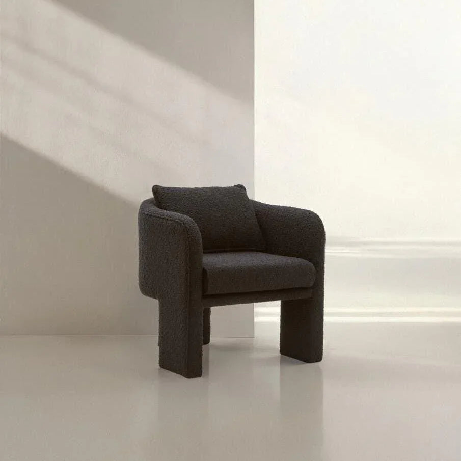 Modern dark fabric armchair with cushioned seat in minimalist room with natural light