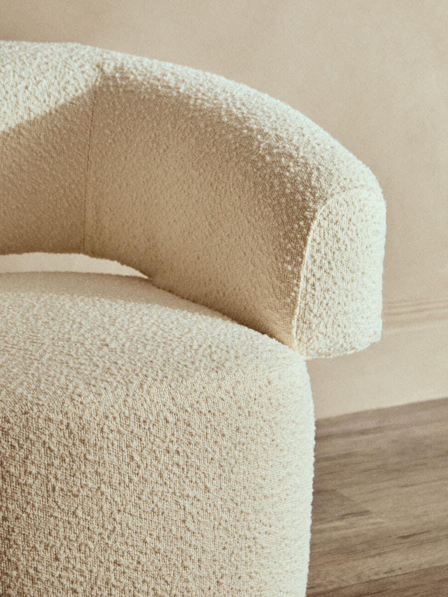 Curved boucle accent chair in cream fabric on wooden floor