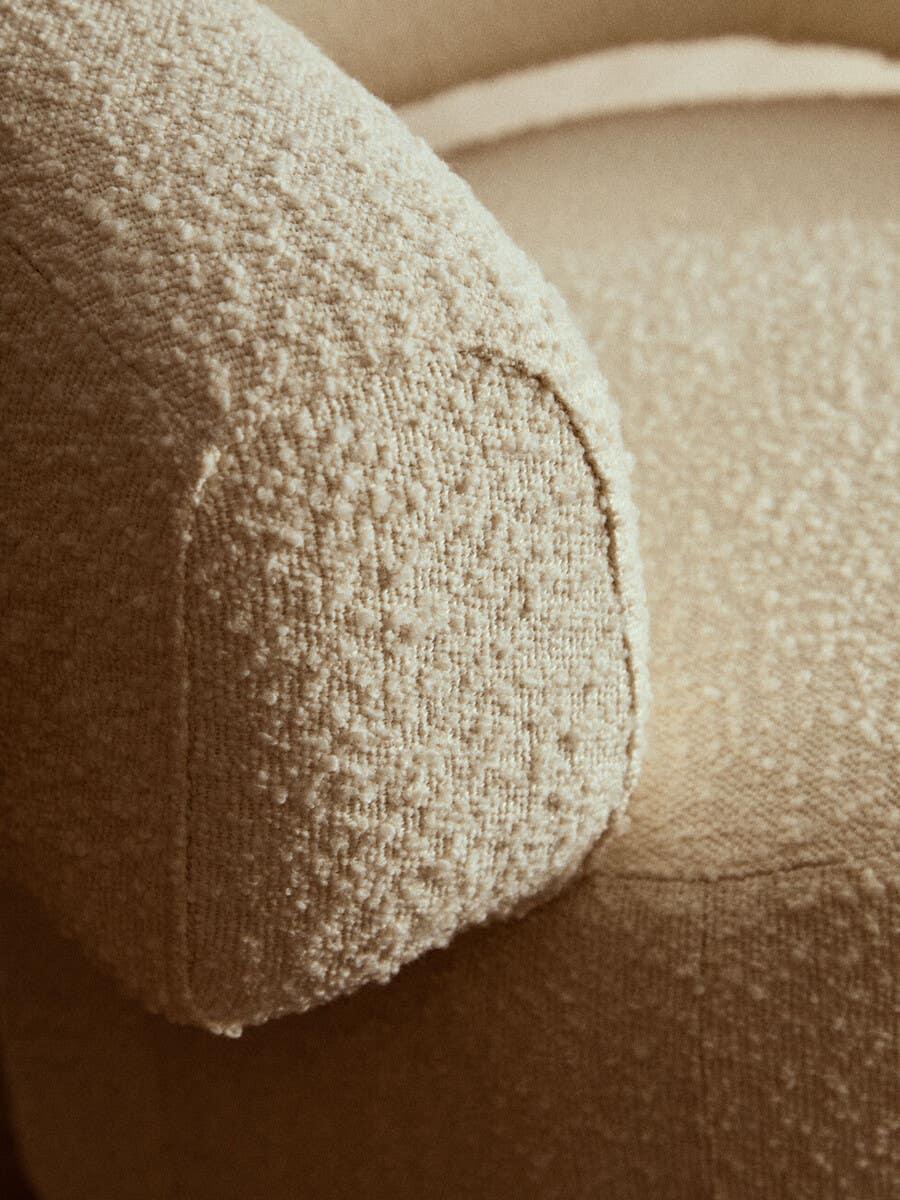 Close-up of beige boucle fabric sofa armrest with textured upholstery