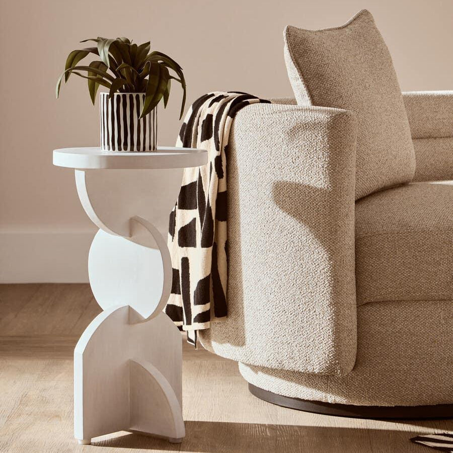 Modern beige sofa with textured upholstery beside sculpted white side table and potted plant