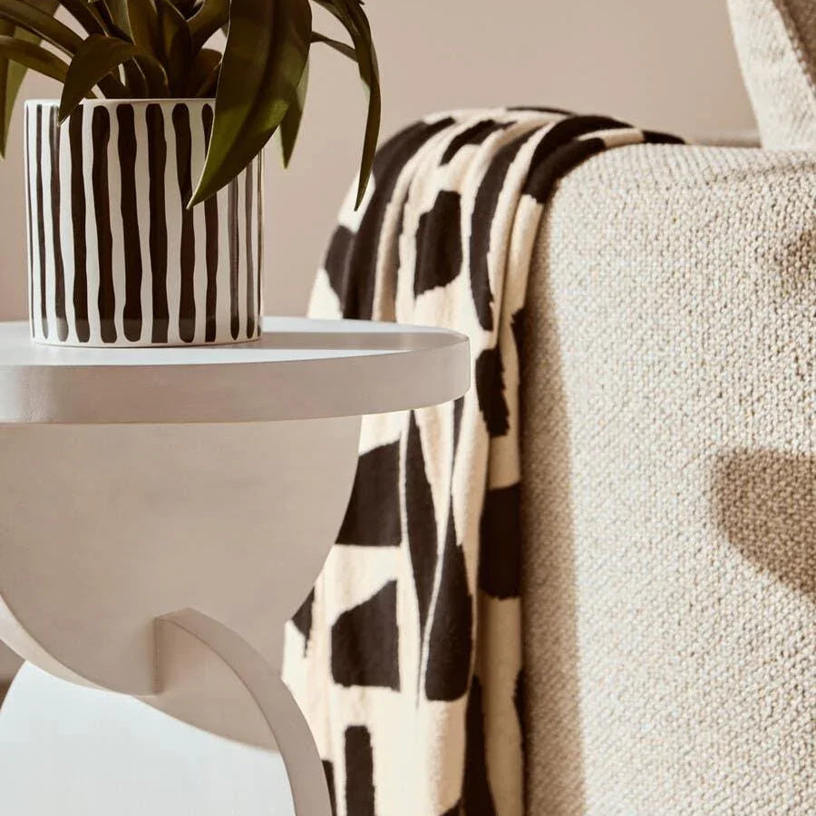 Modern side table with potted plant beside textured beige sofa and patterned throw blanket