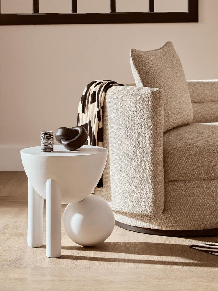 Neutral fabric armchair with accent pillow beside white modern side table on wood floor