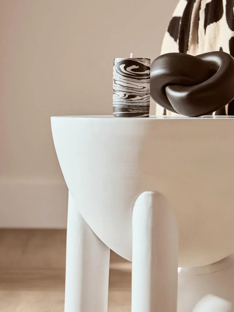 White modern side table with marbled candle and black knot ornament in living room