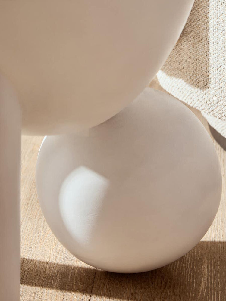 Close-up of modern round ceramic vase on wooden floor near textured beige fabric