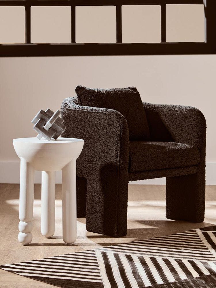 Black boucle armchair with matching cushion beside modern white side table on wooden floor