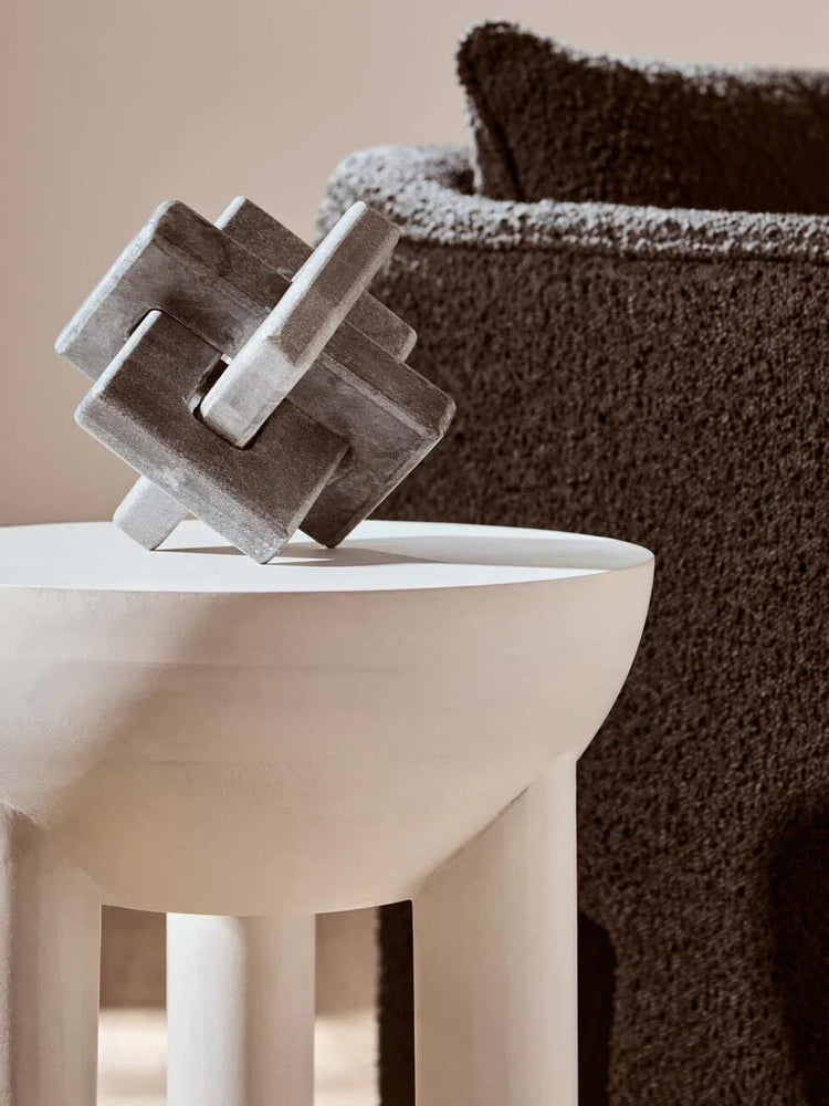 Contemporary white side table with geometric sculpture and textured brown sofa in background