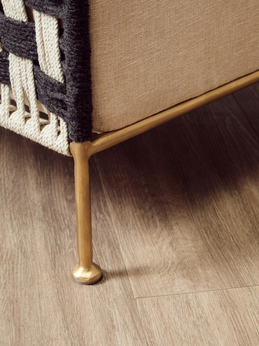 Close-up of sofa metal leg, beige upholstery, braided rope detail, wood floor background