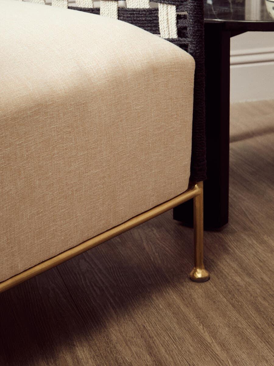 Beige fabric sofa seat with gold metal legs beside a dark wood side table on hardwood floor
