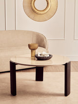 Round cream marble top coffee table with sleek black acacia wood legs, featuring a decorative bowl and a gold glass vase on its surface.