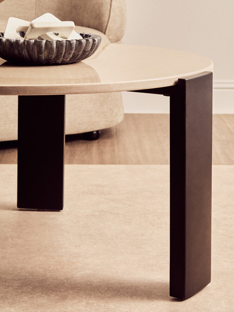 Round cream marble top coffee table featuring sleek black acacia wood legs.