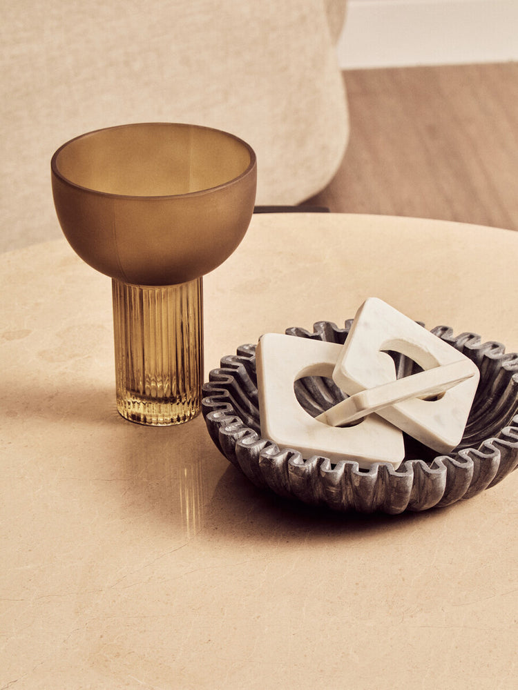 Round cream marble coffee table featuring a smooth surface, complemented by a textured dark bowl holding decorative marble shapes.