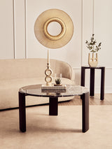 Round coffee table featuring a black and gold marble top with striking white veining, supported by four sturdy black acacia wood legs.
