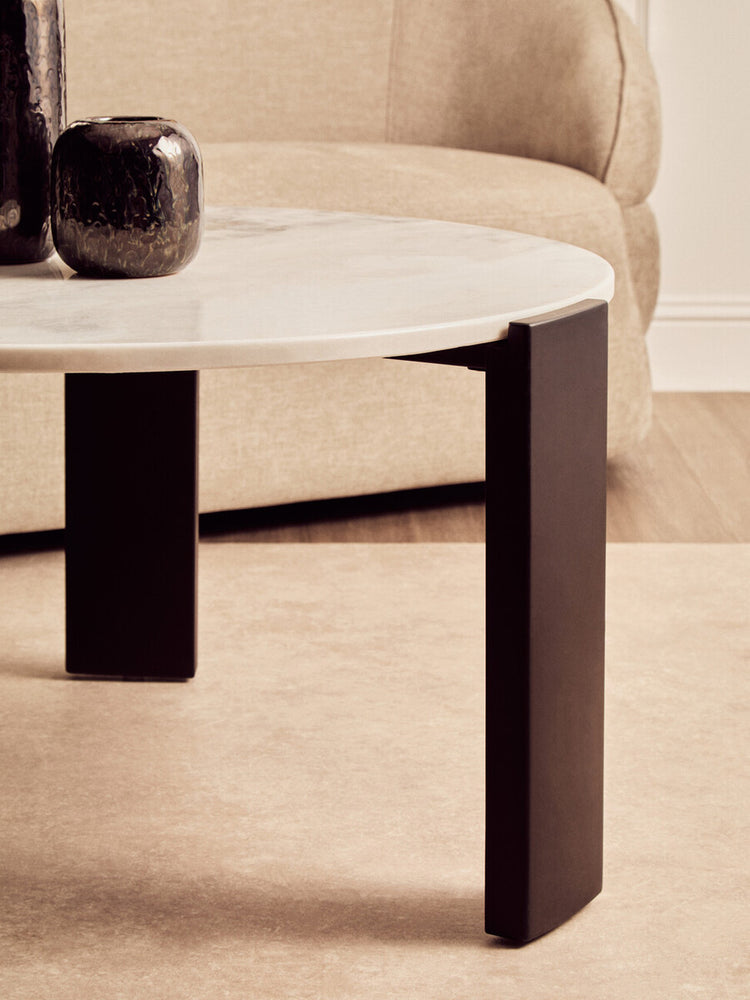 Round coffee table featuring a white marble top with subtle veining, supported by sleek black acacia wood legs.