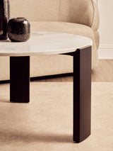Round coffee table featuring a white marble top with subtle veining, supported by sleek black acacia wood legs.
