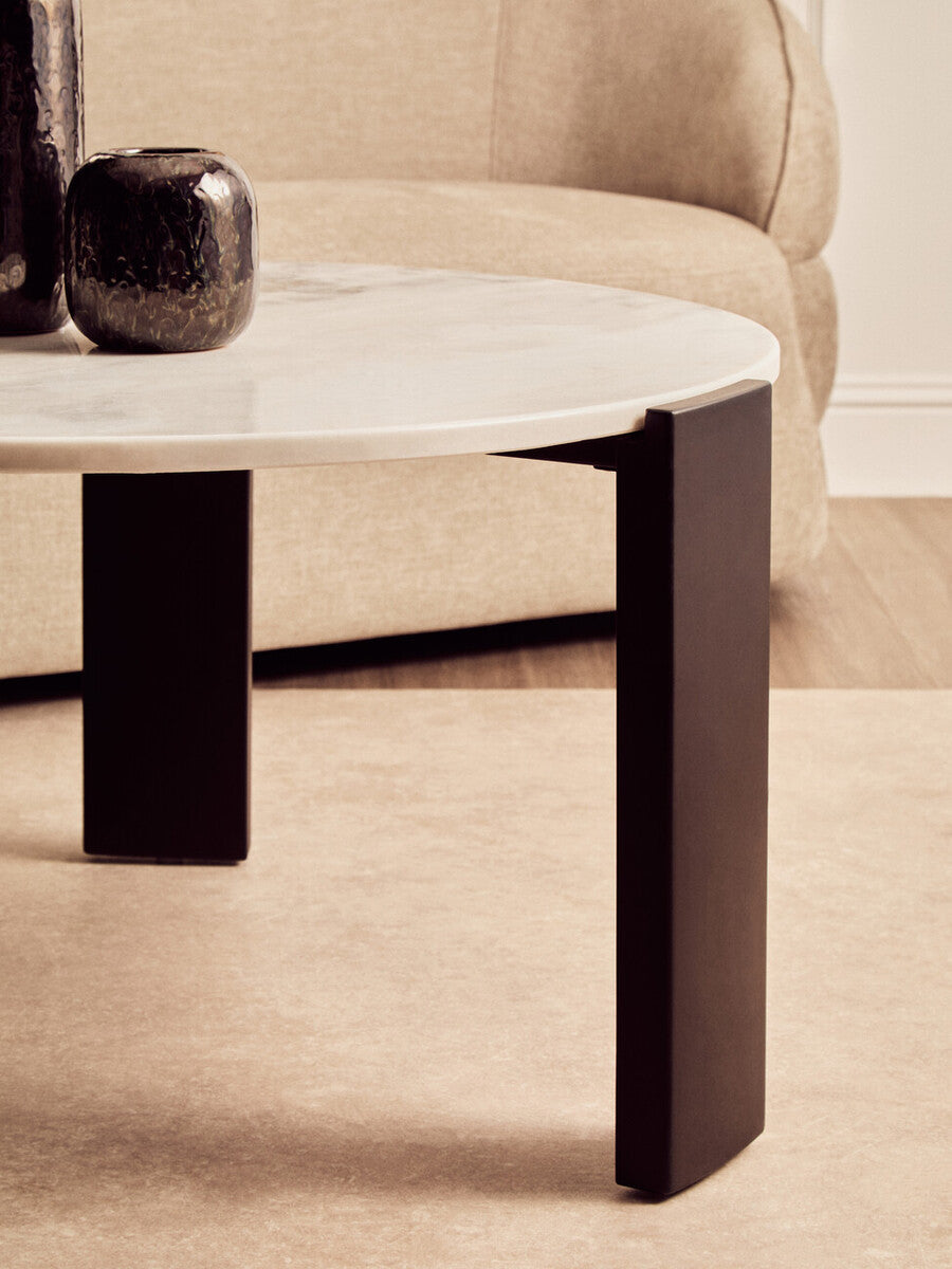 Round coffee table featuring a white marble top with subtle veining, supported by sleek black acacia wood legs.