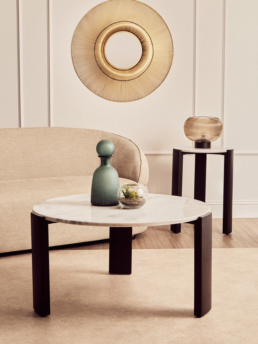 Round coffee table featuring a white marble top with subtle gray veining, supported by sleek black acacia wood legs.