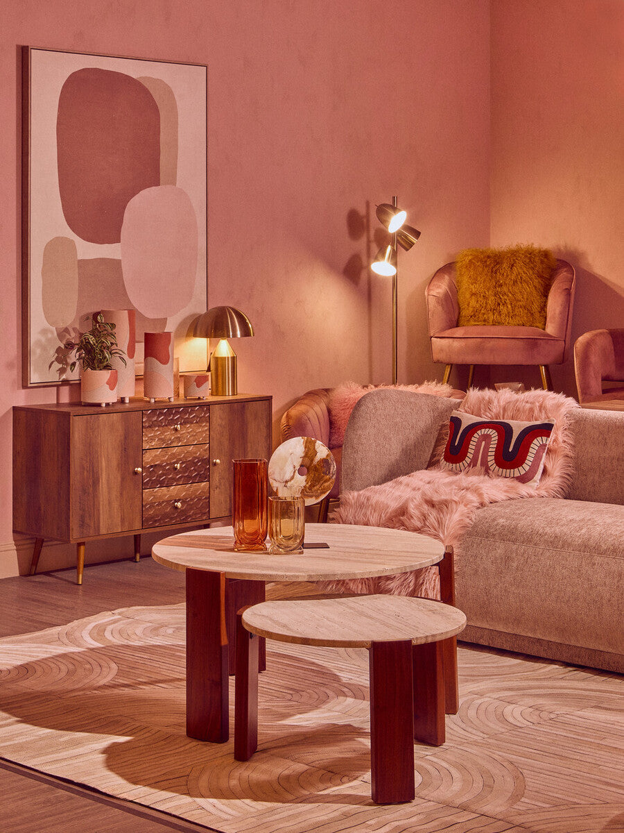 Round coffee table featuring a cream travertine marble top and acacia wood legs, set in a stylish living room with a pink wall backdrop.