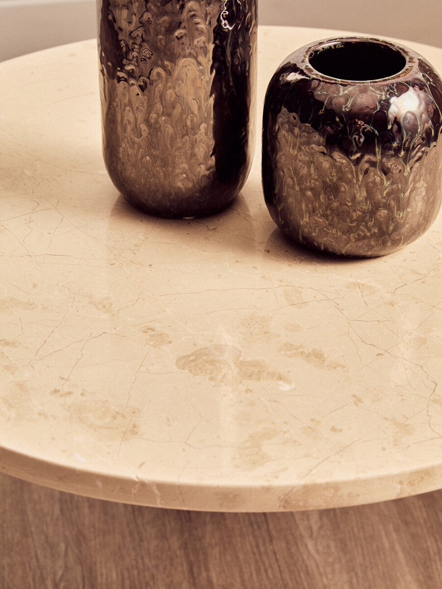 Round cream marble top coffee table featuring a smooth surface with subtle veining, complemented by two dark, glossy vases.