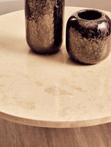 Round cream marble top coffee table featuring a smooth surface with subtle veining, complemented by two dark, glossy vases.