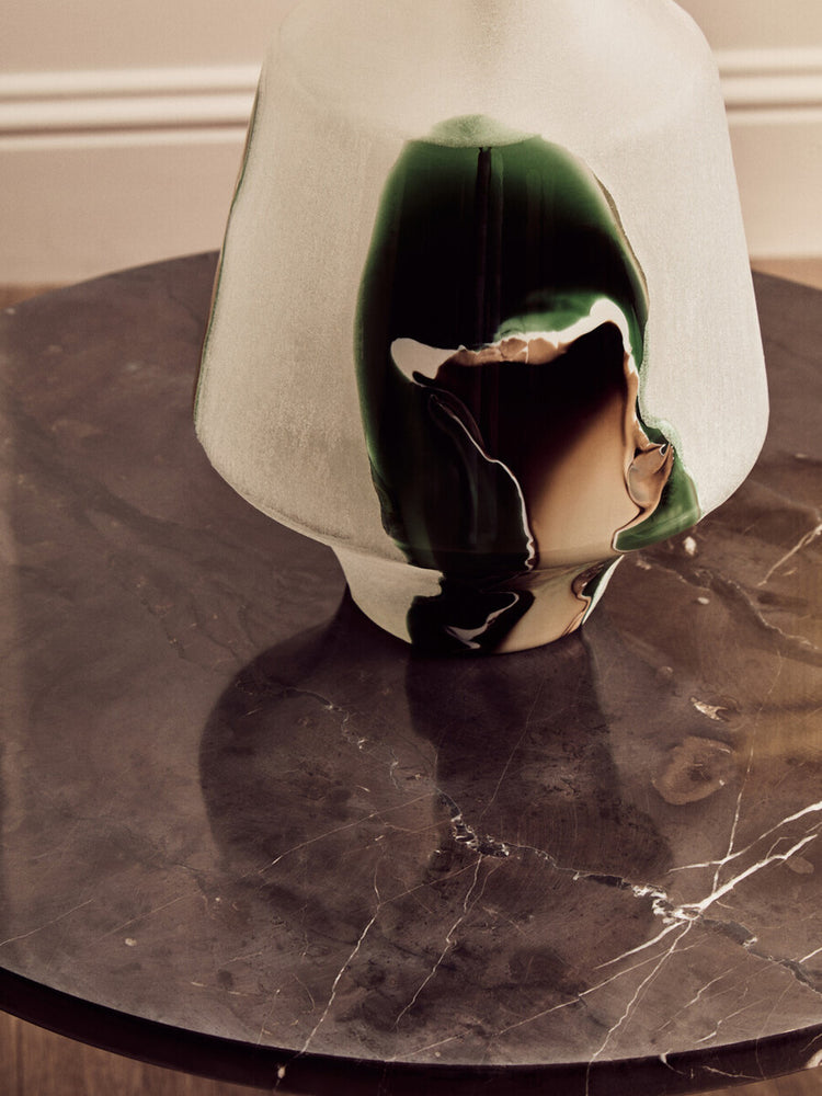 Round black marble top coffee table featuring a smooth surface with subtle veining, complemented by a stylish glass vase with green and brown accents.