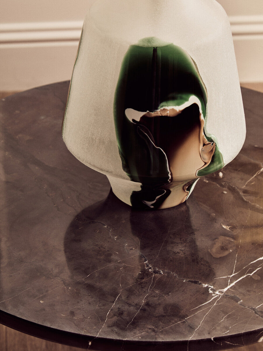 Round black marble top coffee table featuring a smooth surface with subtle veining, complemented by a stylish glass vase with green and brown accents.