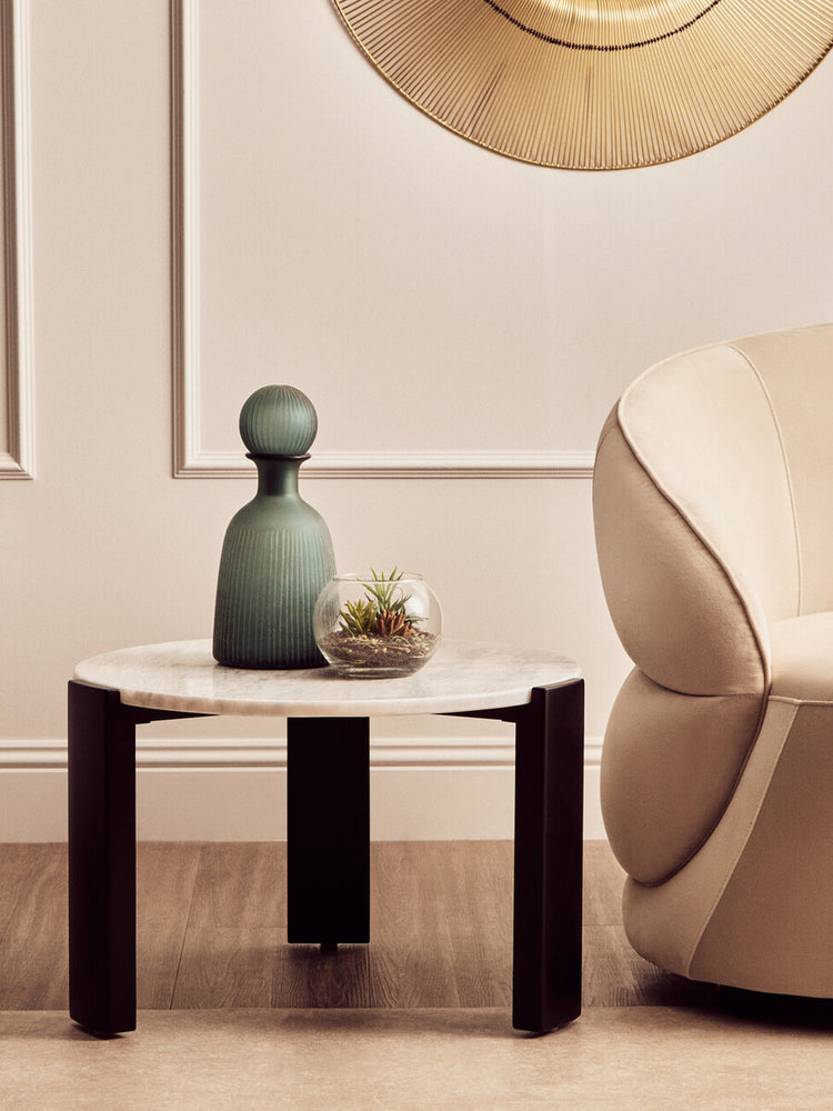 Round coffee table featuring a white marble top and sleek black acacia wood legs, styled with a green decorative vase and a small glass terrarium.