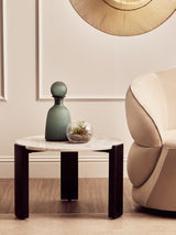 Round coffee table featuring a white marble top and sleek black acacia wood legs, styled with a green decorative vase and a small glass terrarium.