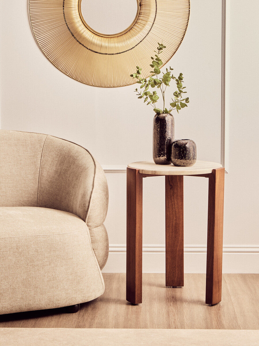 Round side table featuring a smooth travertine top and sturdy acacia wood legs, set beside a plush beige sofa.