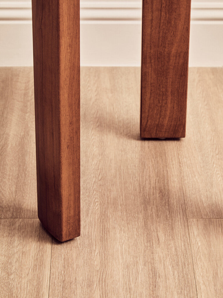 Close-up view of a sturdy, brown acacia wood leg of a round side table, showcasing its smooth finish and slightly rounded edges, set against a light wooden floor.