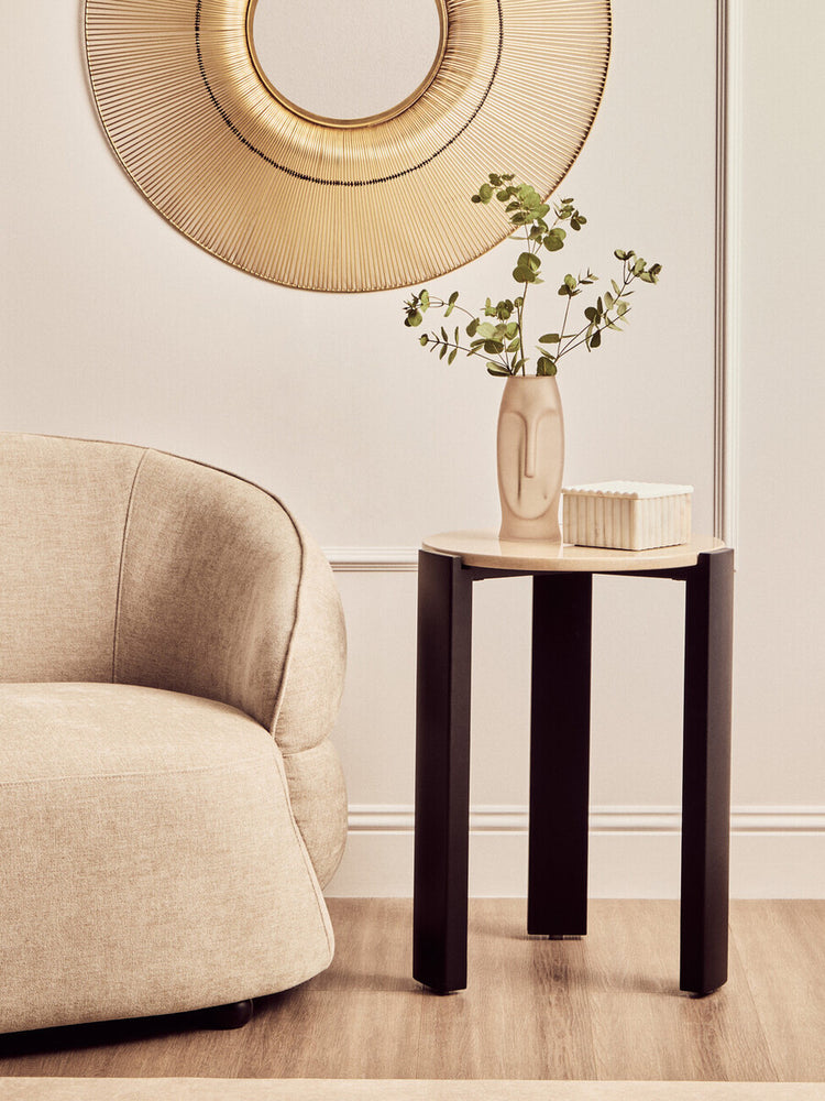 Round side table featuring a cream marble top and sleek black acacia wood legs, positioned next to a soft beige upholstered sofa.