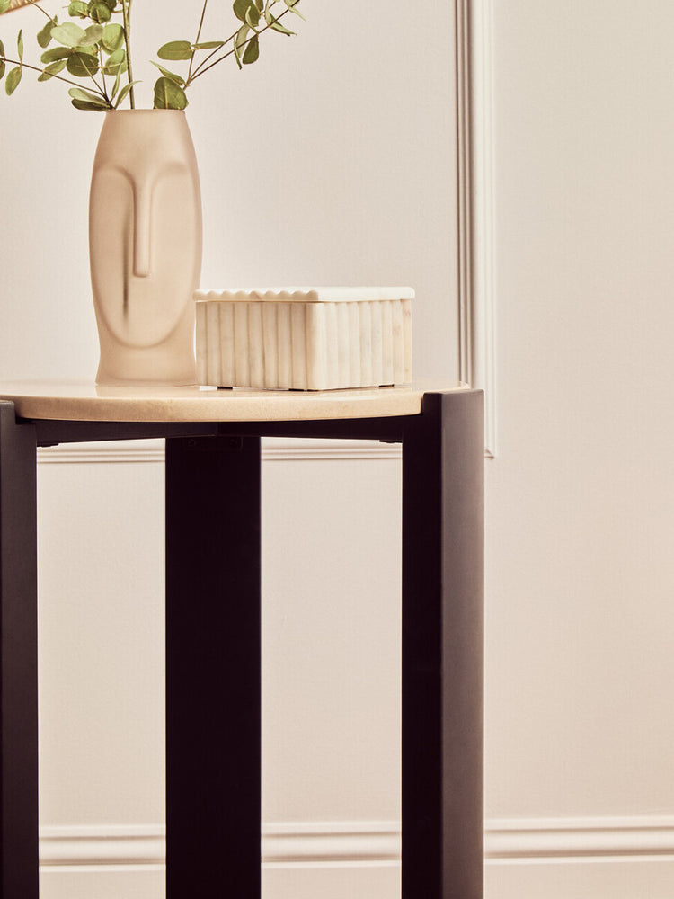 Round side table featuring a cream marble top and sleek black acacia wood legs.