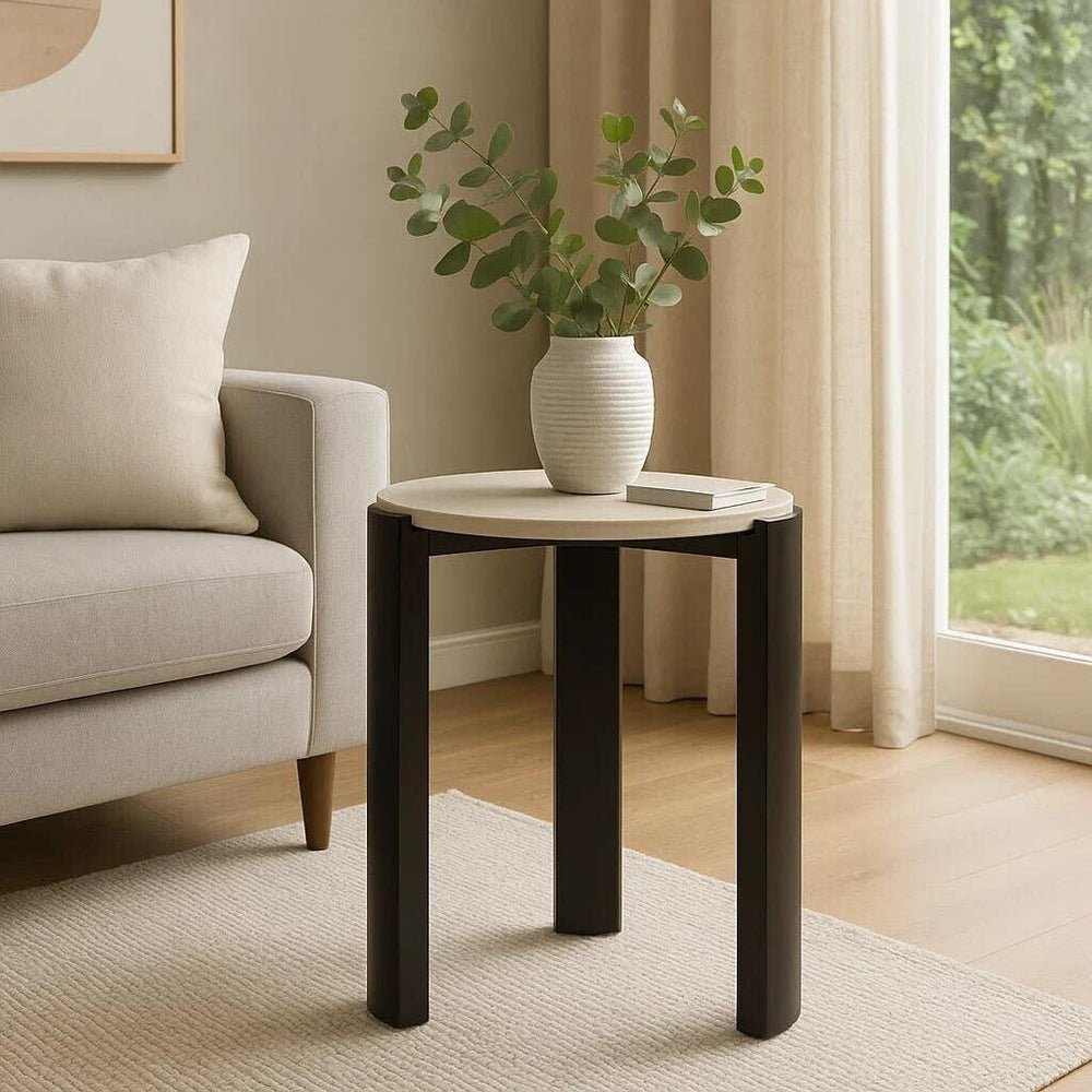 Modern round side table with dark legs and light top beside sofa, vase and book on table