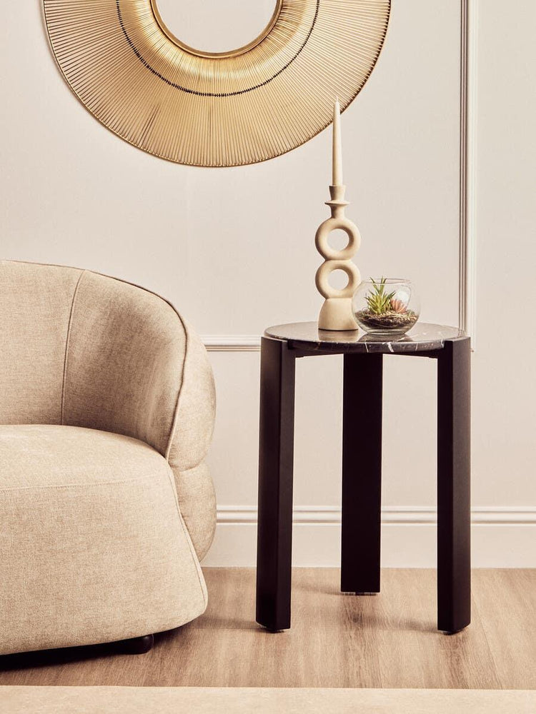 Black marble side table with decorative candle and plant beside beige sofa in modern living room