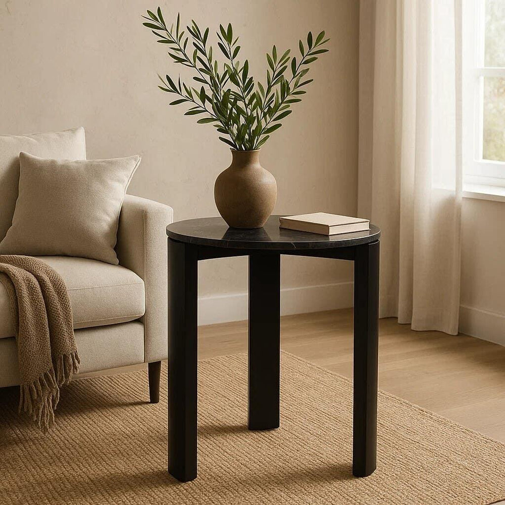Black round side table with vase and book beside beige sofa in modern living room