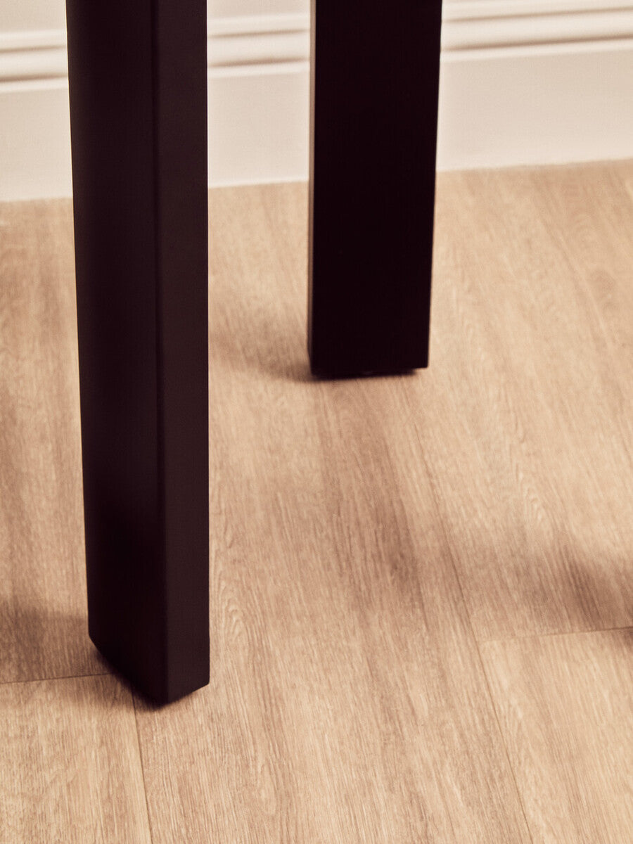 Close-up view of a black wooden leg of a round side table, showcasing its clean lines and sturdy design.
