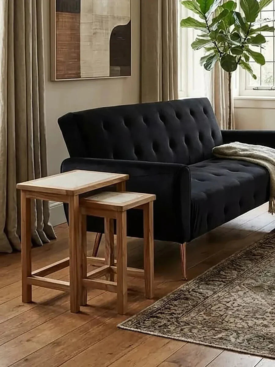 Black tufted sofa with wooden nesting tables in a modern living room with plant and rug