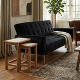 Black velvet sofa with button tufting beside wooden nesting tables in a stylish living room