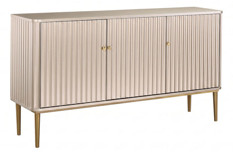 Elegant sideboard featuring three doors with a distinctive flute detail, finished in a soft gold hue. The piece is supported by slender, tapered legs in a matching gold tone.
