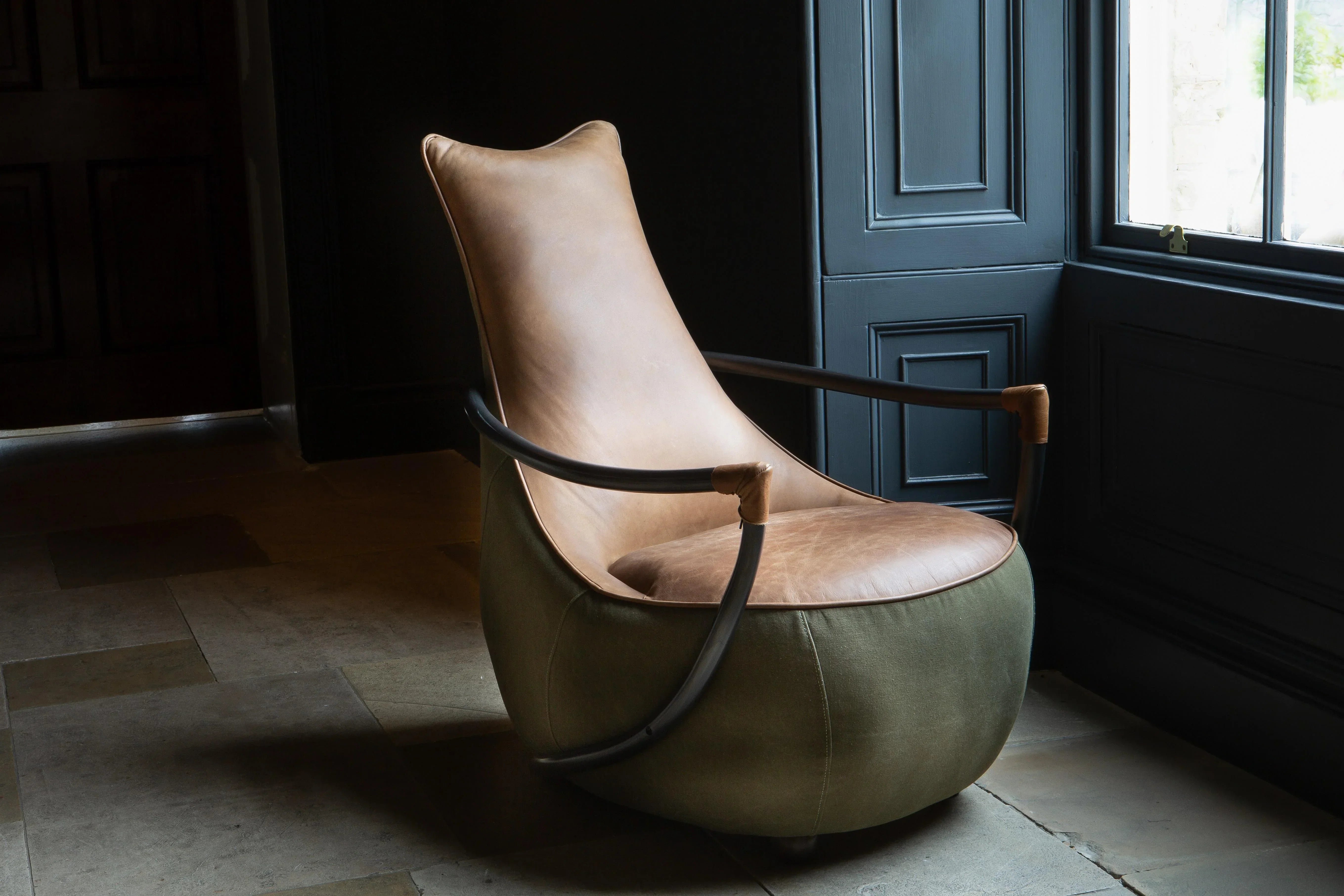 Modern accent chair with tan leather seat, curved black arms, and olive green fabric base