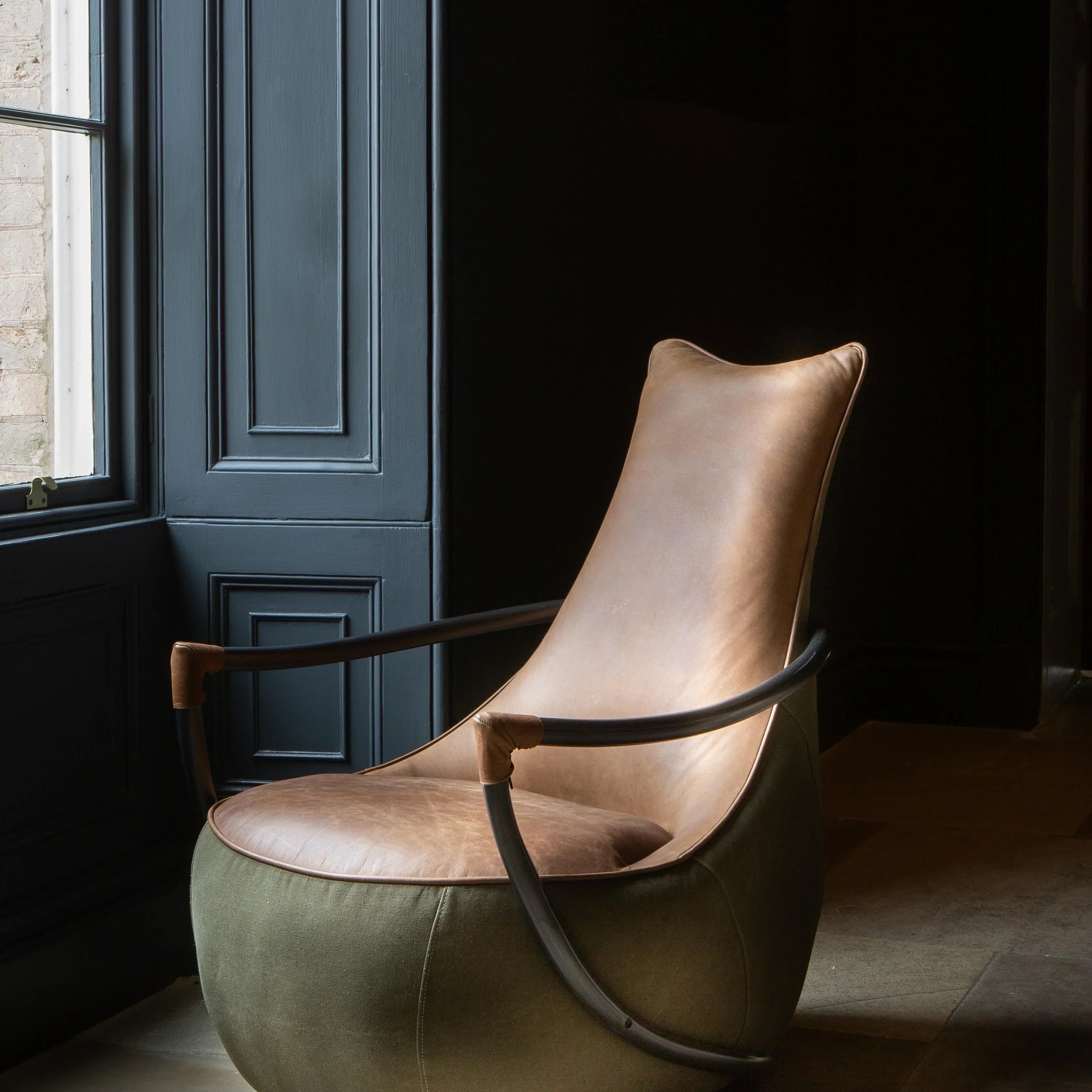 Modern accent armchair with tan leather seat, metal frame, and olive green fabric base