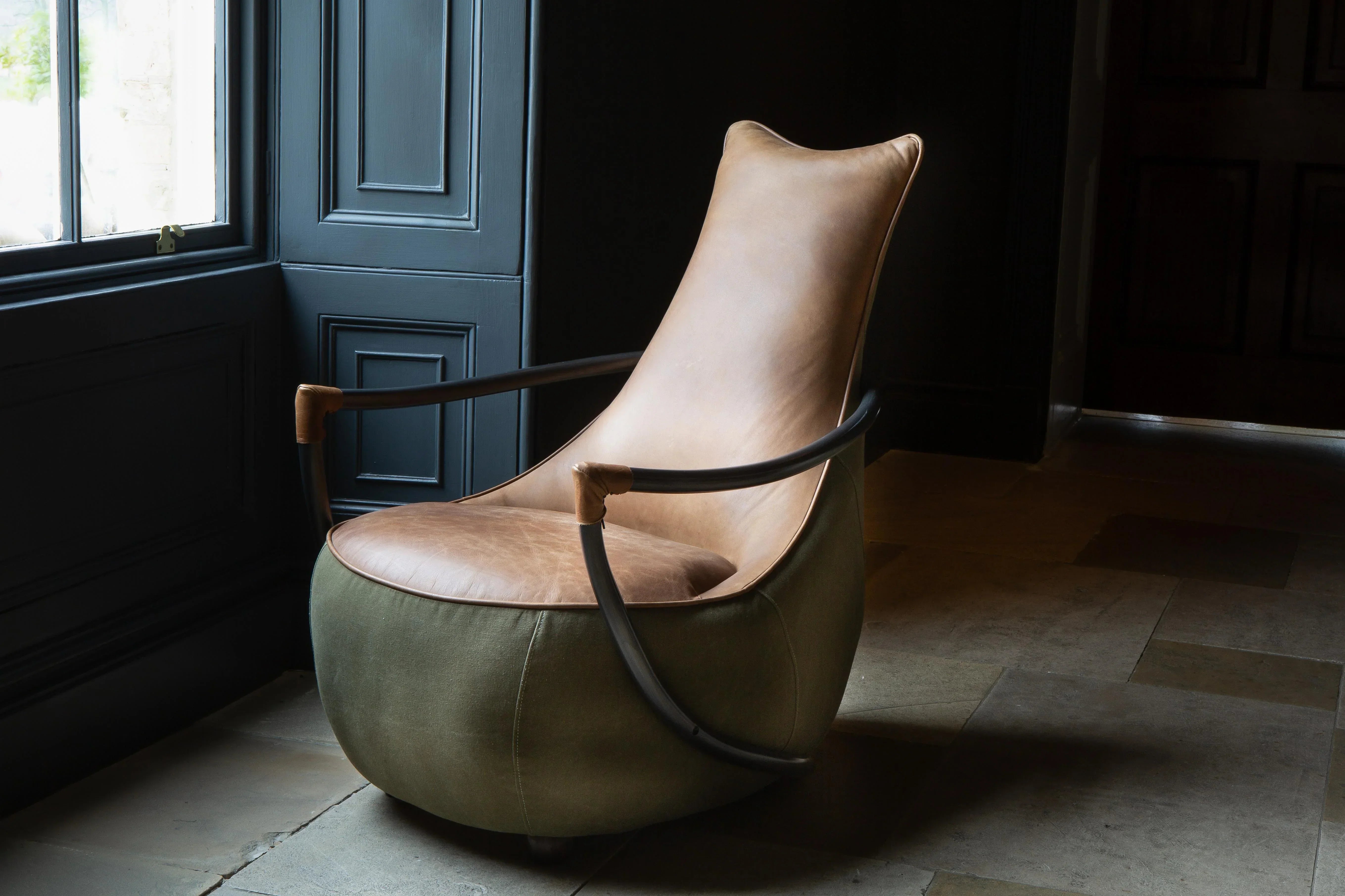 Leather accent chair with curved black metal arms and green upholstered base by a window