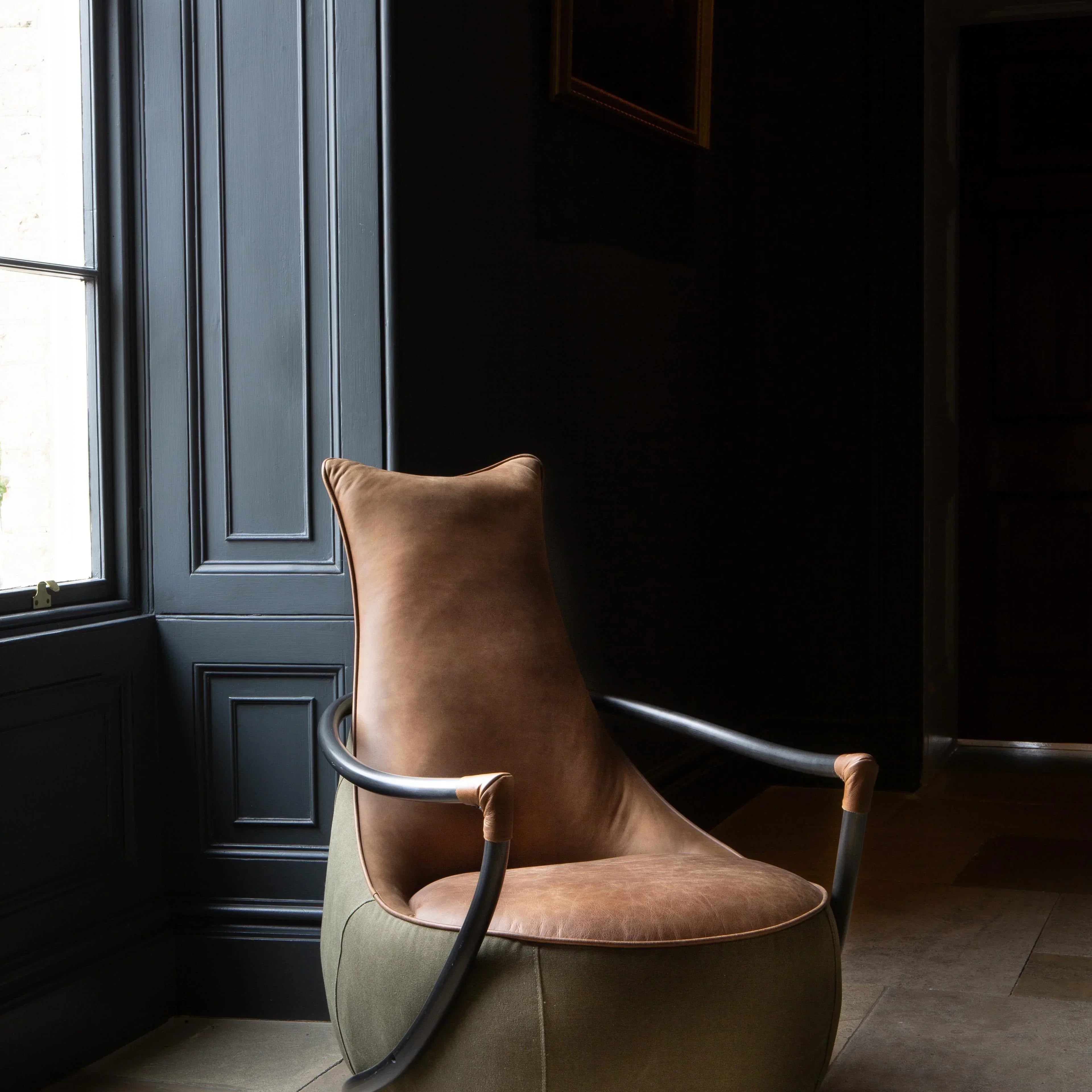 Brown leather accent chair with metal arms next to a window in a modern living room