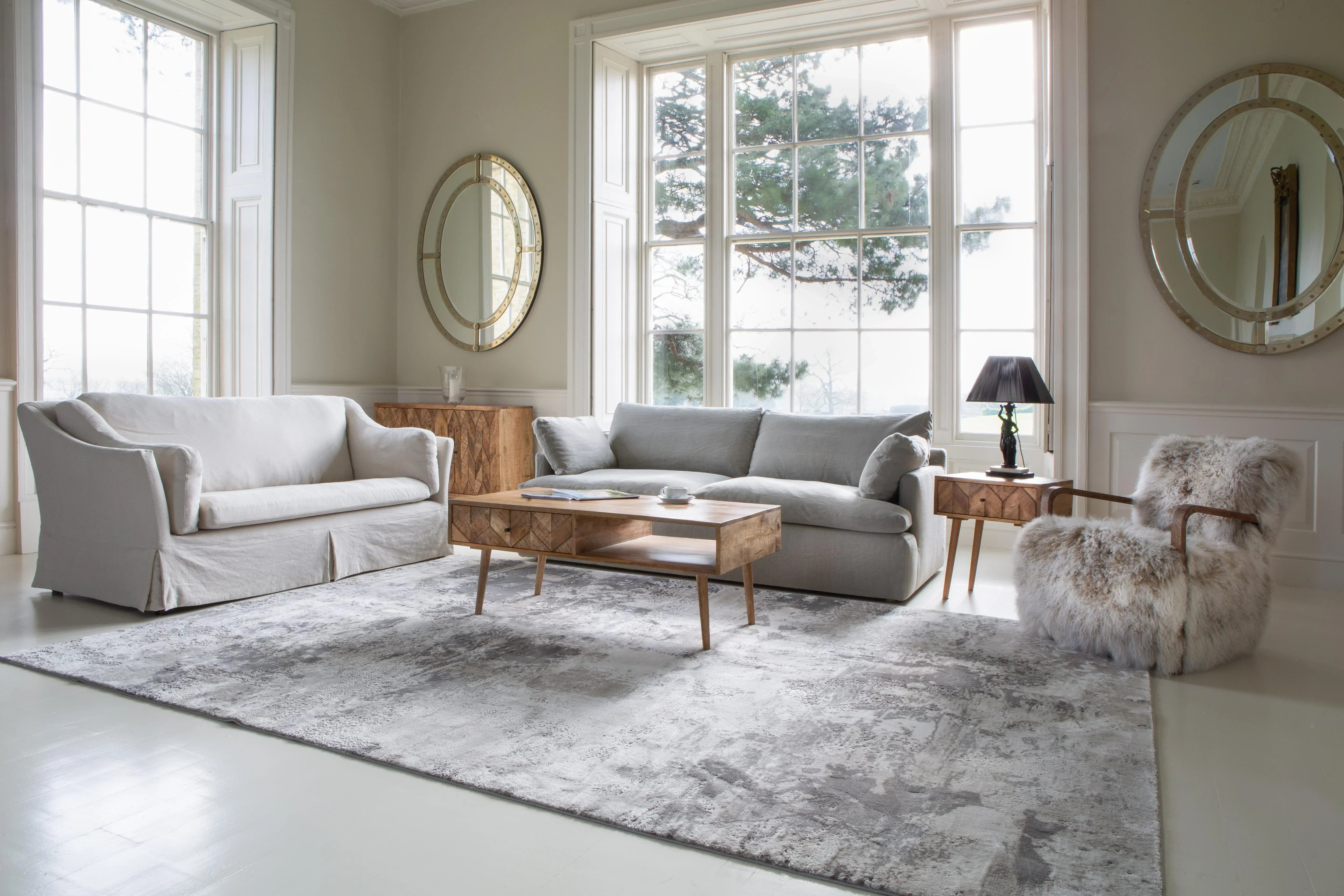 Neutral living room with grey sofa, wooden coffee table, plush armchair, large rug